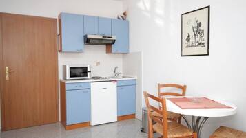 A compact kitchen with blue cabinets, a microwave, and a sink. There is a dining table with two chairs and a framed picture on the wall.