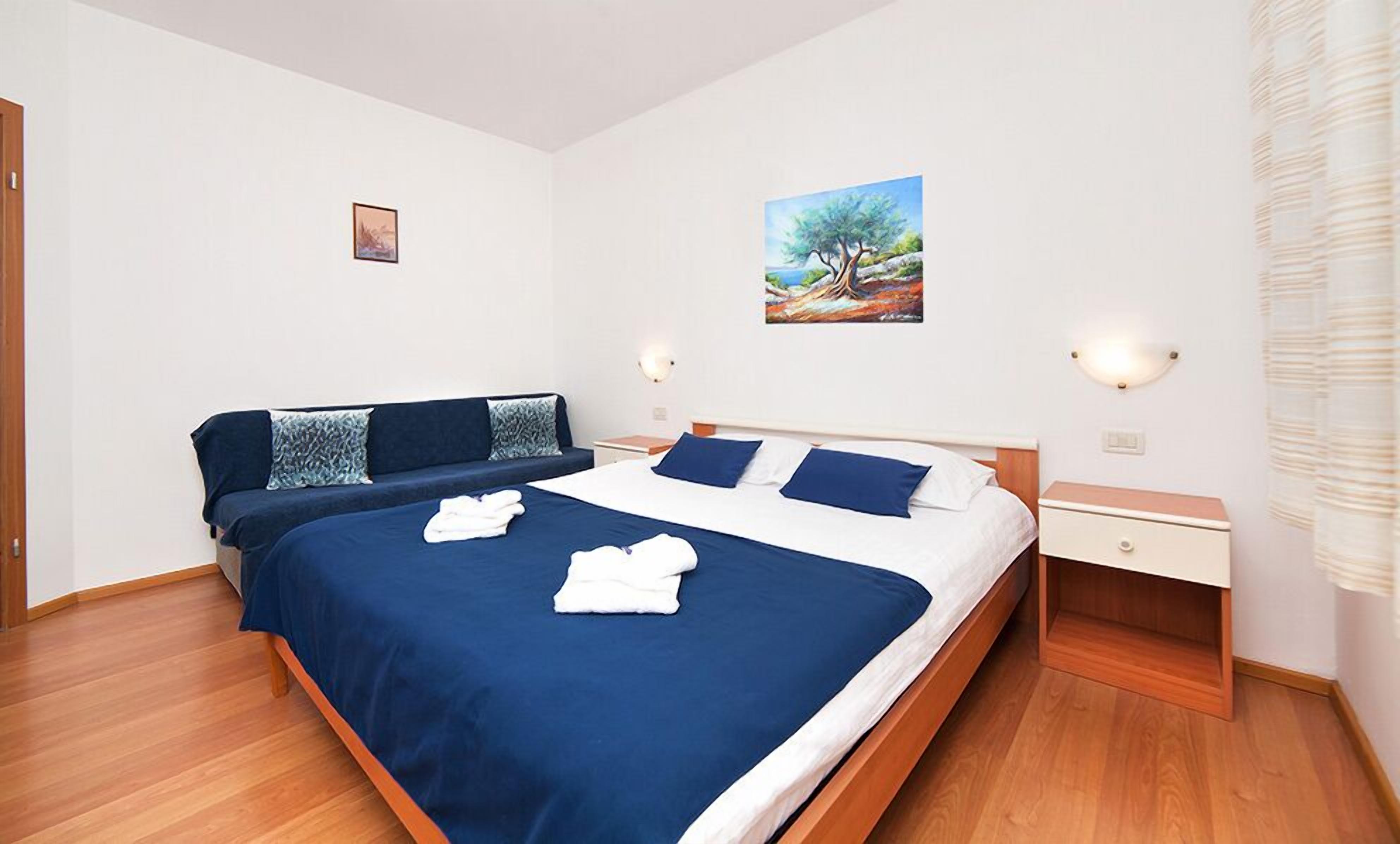 Ein Schlafzimmer mit einem großen Bett, einem Schlafsofa, einem Nachttisch und einem Bild an der Wand.