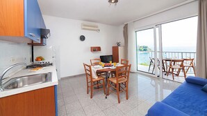 A modern kitchen with a sink and stove, a dining area with a table and chairs, a TV, and a balcony with a view of the sea. - Villa Lidija (Lovran)
