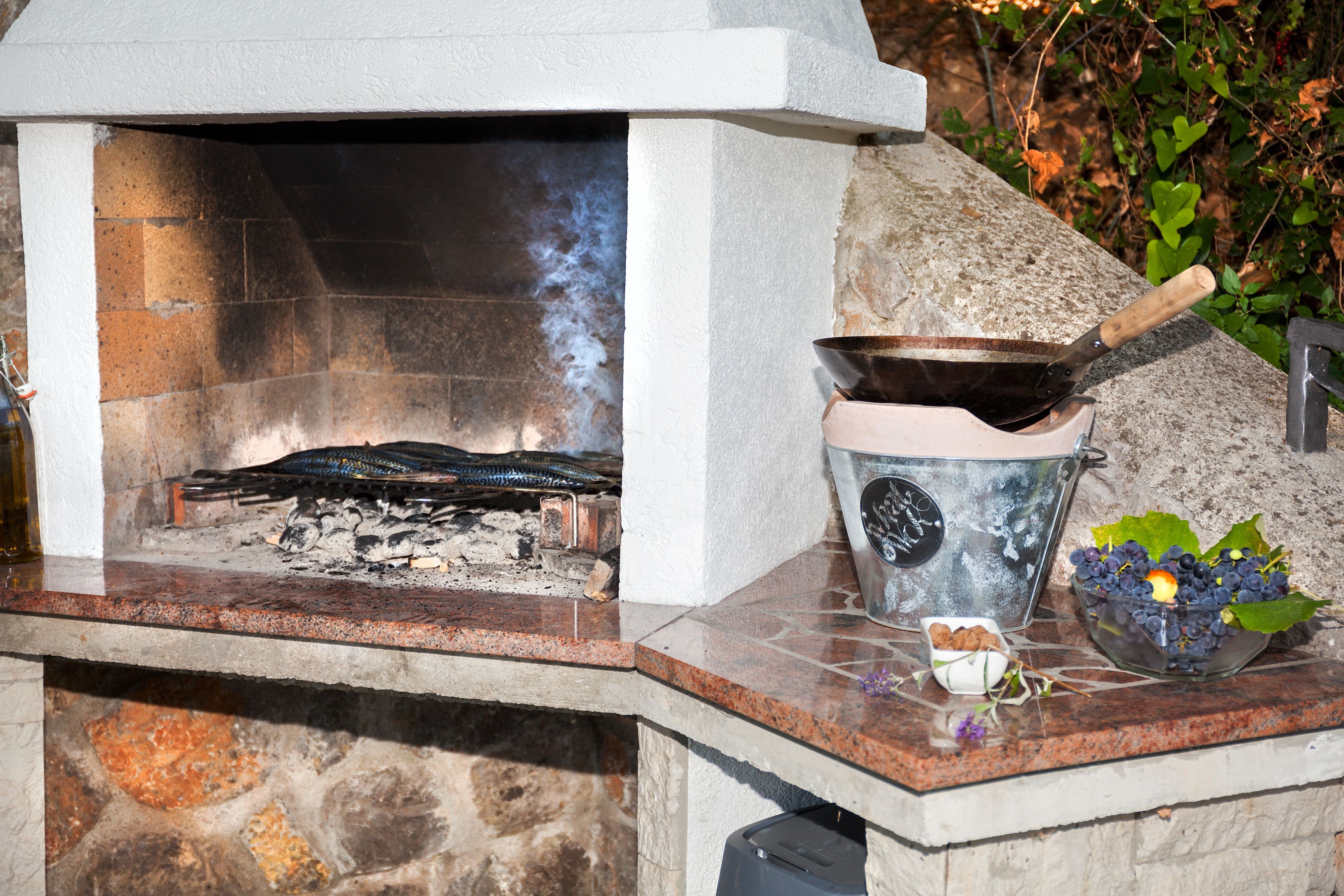 A stone fireplace with a metal cooking pot and a bowl of fruit on the mantel.