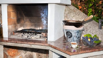 A stone fireplace with a metal cooking pot and a bowl of fruit on the mantel.