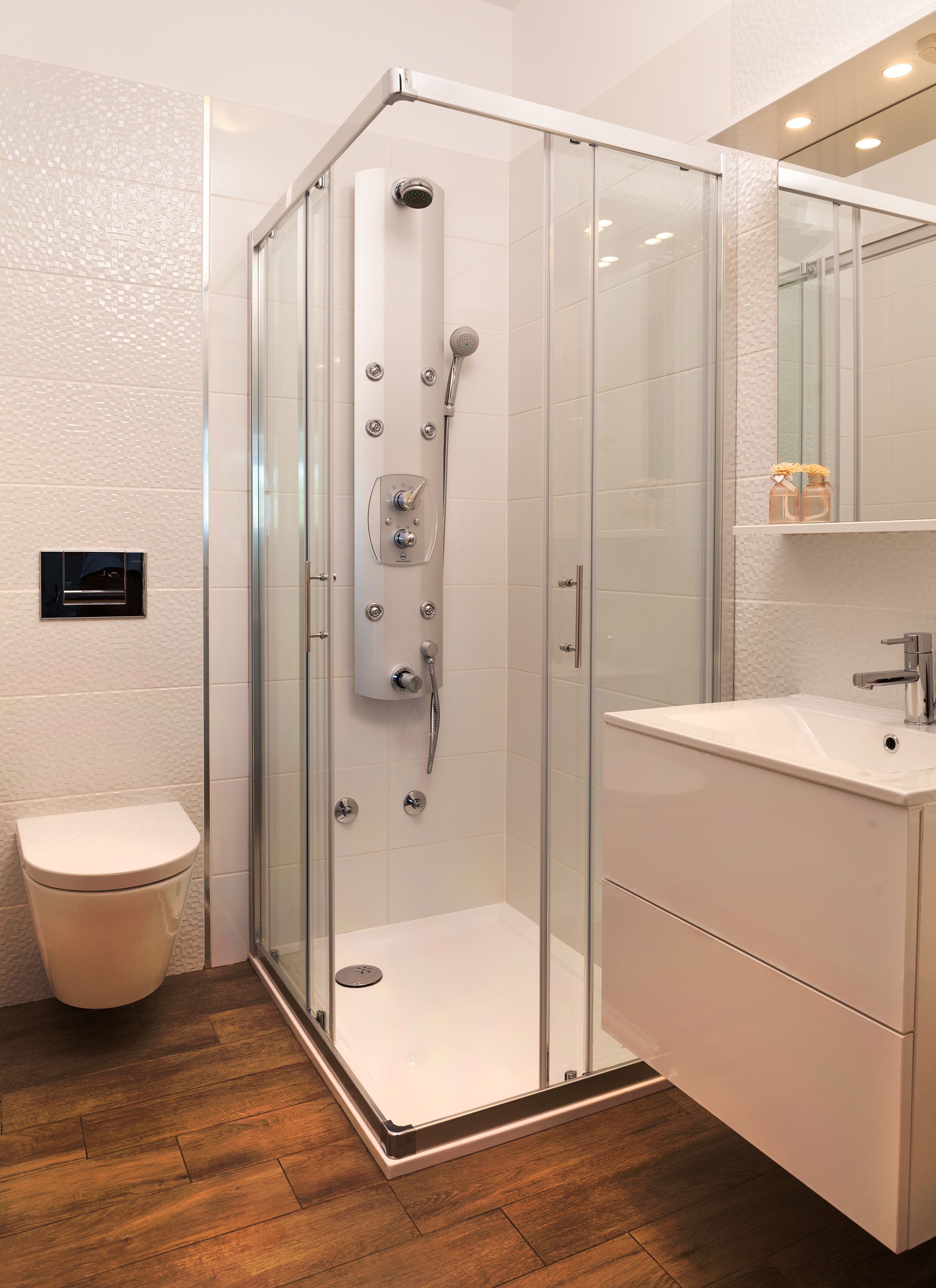 A modern bathroom with a glass-enclosed shower, a toilet, and a sink with a mirror above.