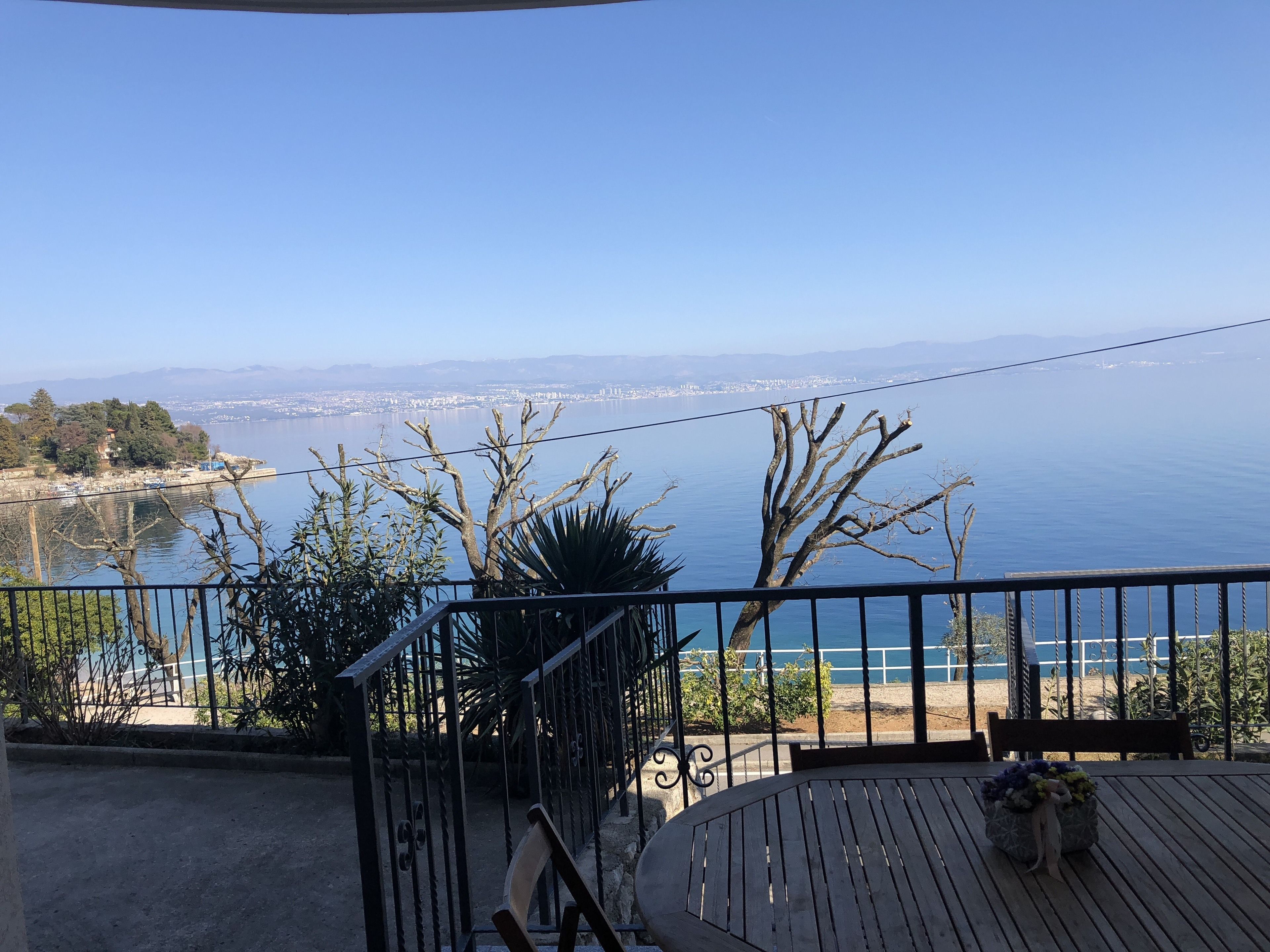 A balcony with a view of the sea and a distant cityscape.
