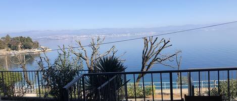 A balcony with a view of the sea and a distant cityscape.
