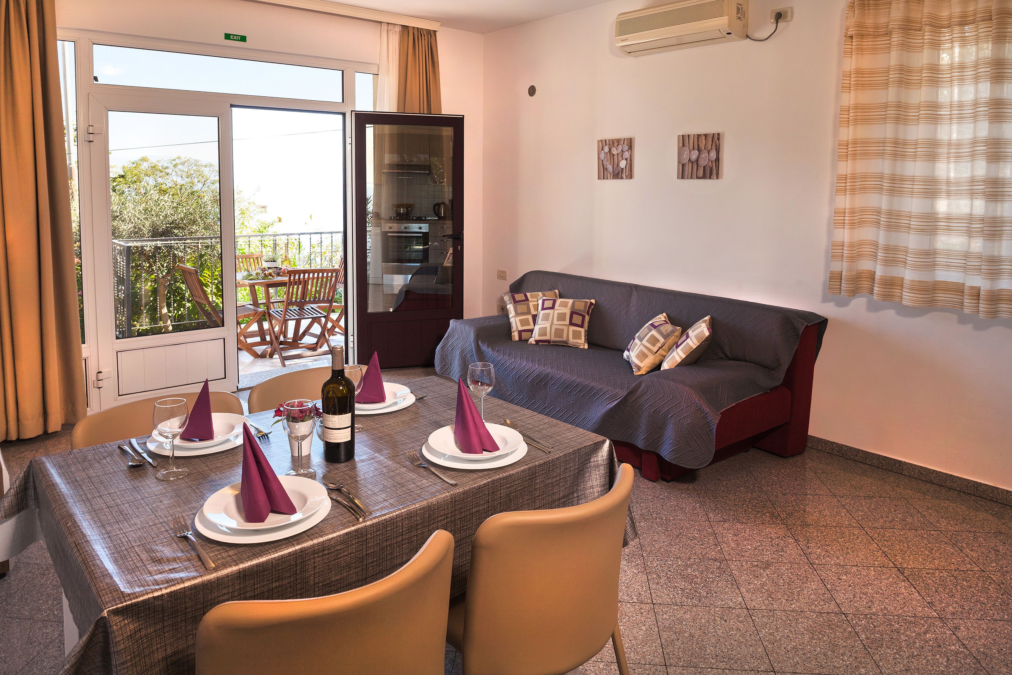 A dining area with a table set for two, a sofa, and a sliding glass door leading to a balcony.