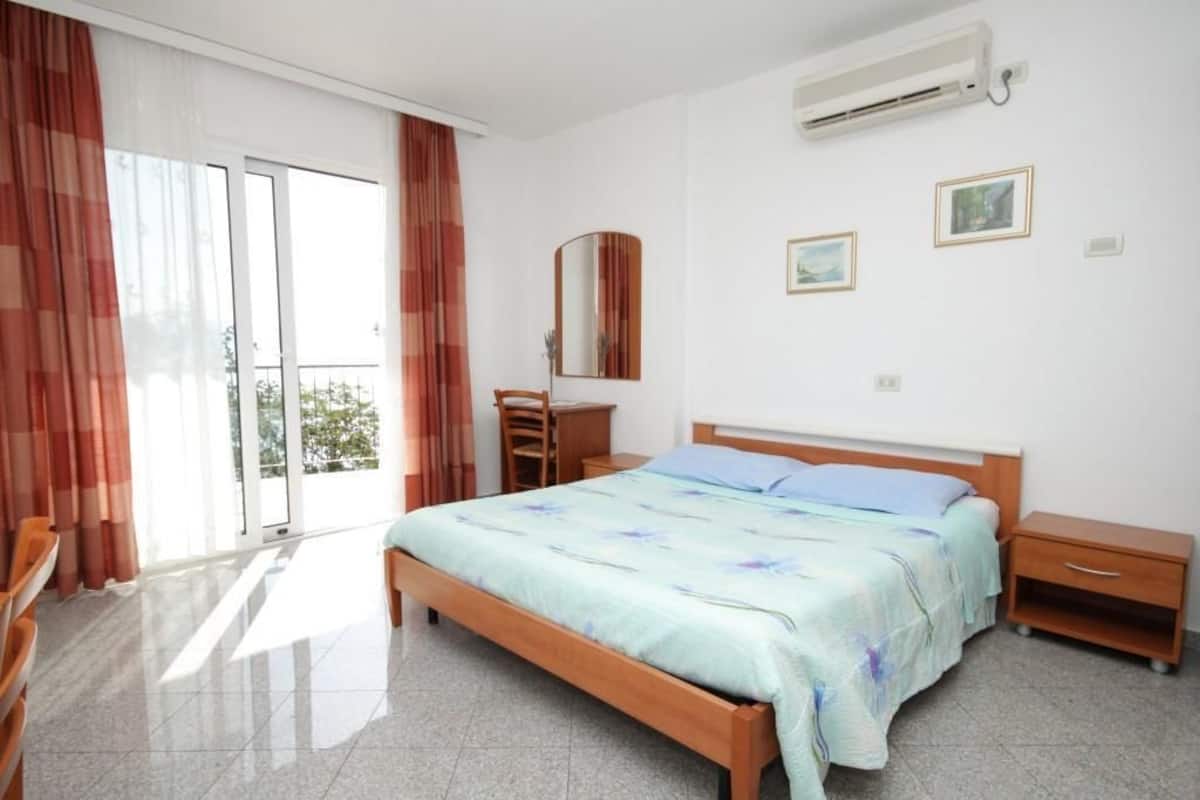 A bedroom with a bed, a nightstand, a dresser, a mirror, and a sliding glass door to a balcony.