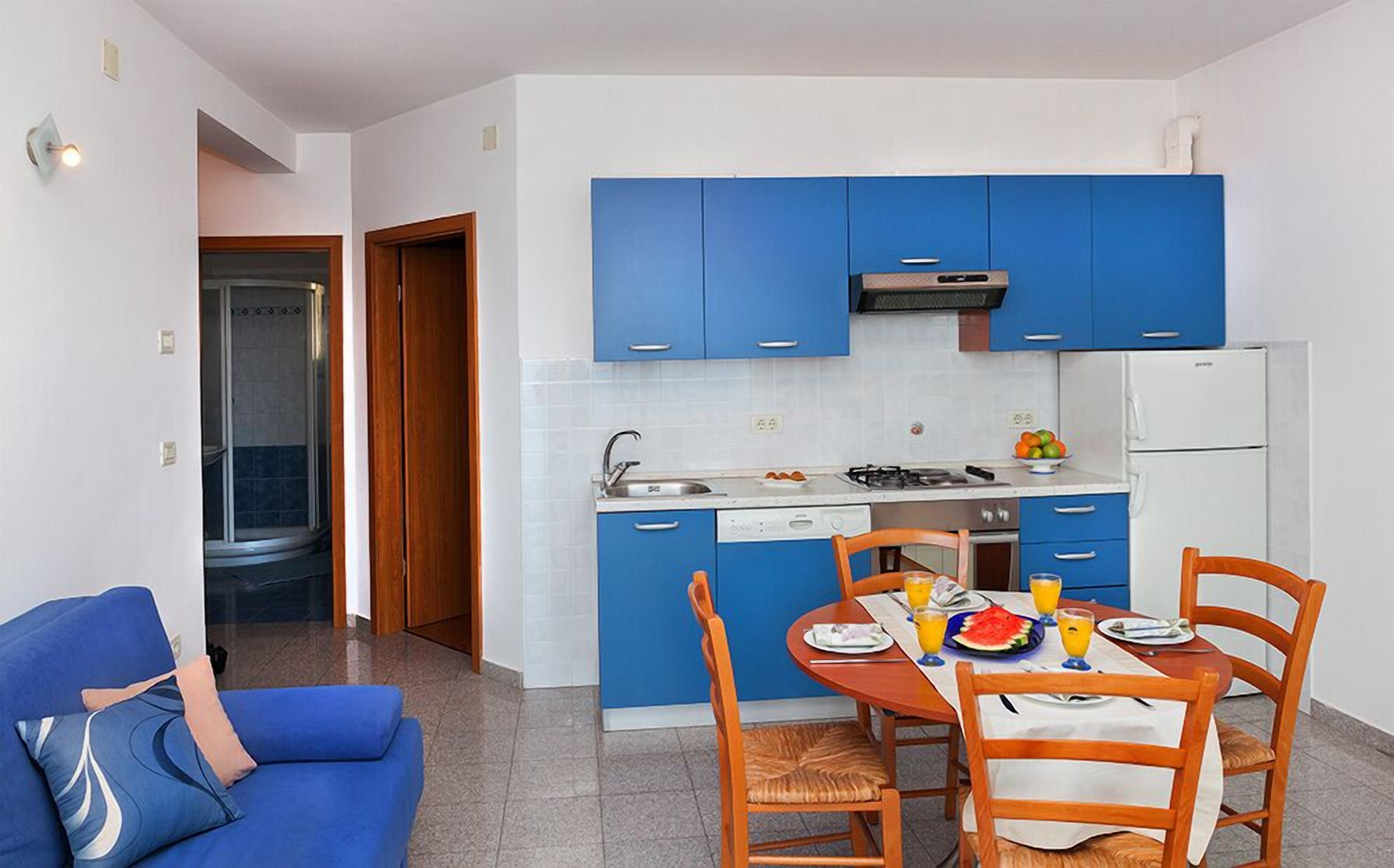 Une cuisine de taille réduite avec des meubles bleus, une table à manger avec quatre chaises et un réfrigérateur.