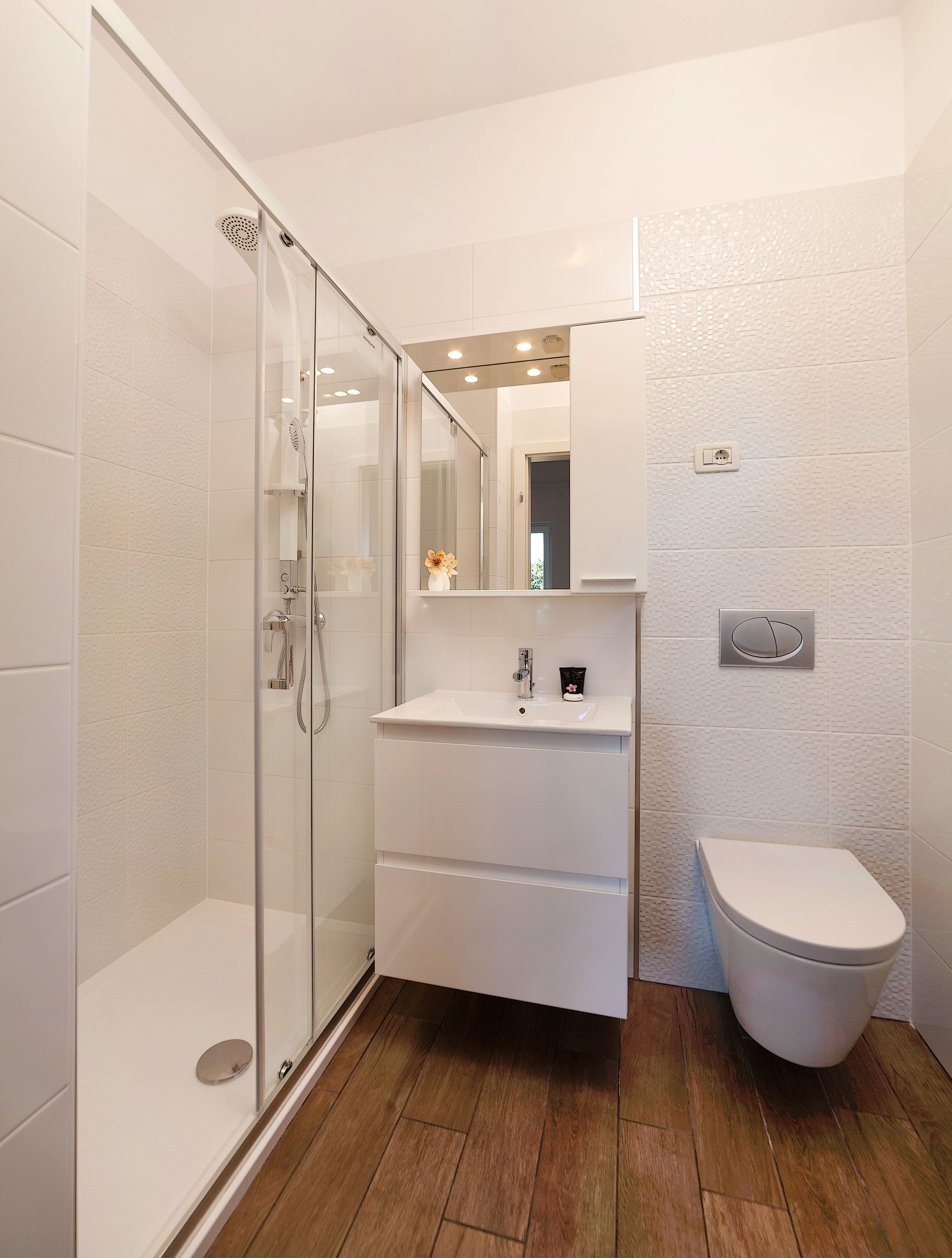 A modern bathroom with a glass shower enclosure, a white sink with a mirror above it, and a toilet.