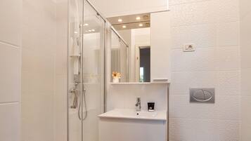 A modern bathroom with a glass shower enclosure, a white sink with a mirror above it, and a toilet.