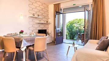 A modern hotel room with a dining area, a sofa, and a balcony with a view of greenery.