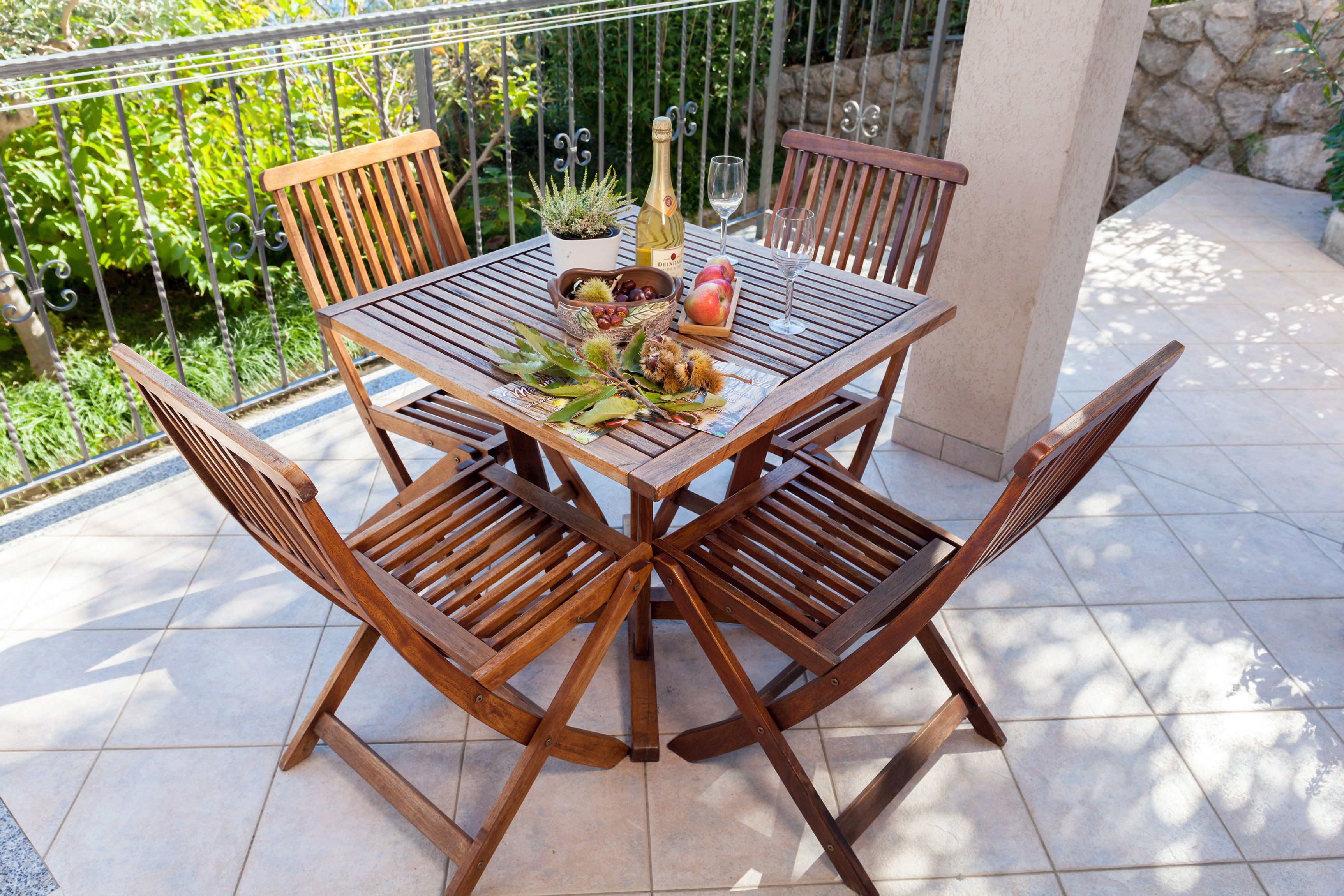 Una mesa de madera con cuatro sillas, una botella de vino, una copa y un cuenco de fruta en un patio empedrado.