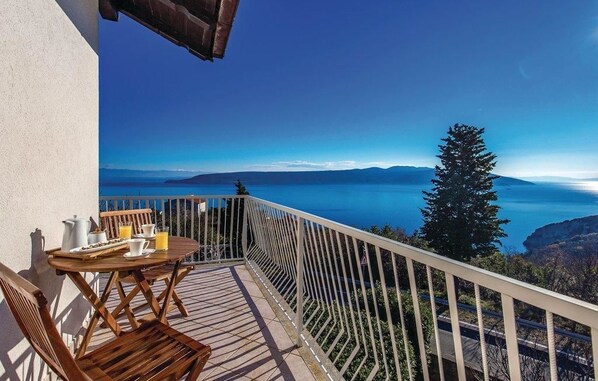 Ein Balkon mit Holztisch, gedeckt für das Frühstück, mit Blick auf eine malerische Seen- und Berglandschaft.