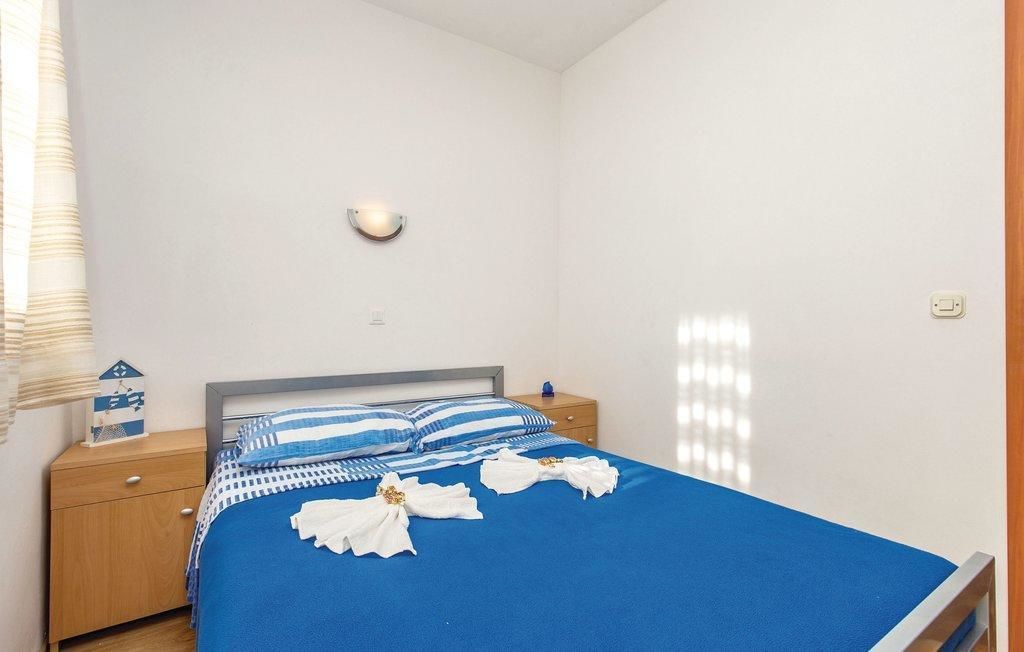 Ein Schlafzimmer mit einem Bett, einem Nachttisch, einer Wandleuchte und einem Fenster mit Jalousien.