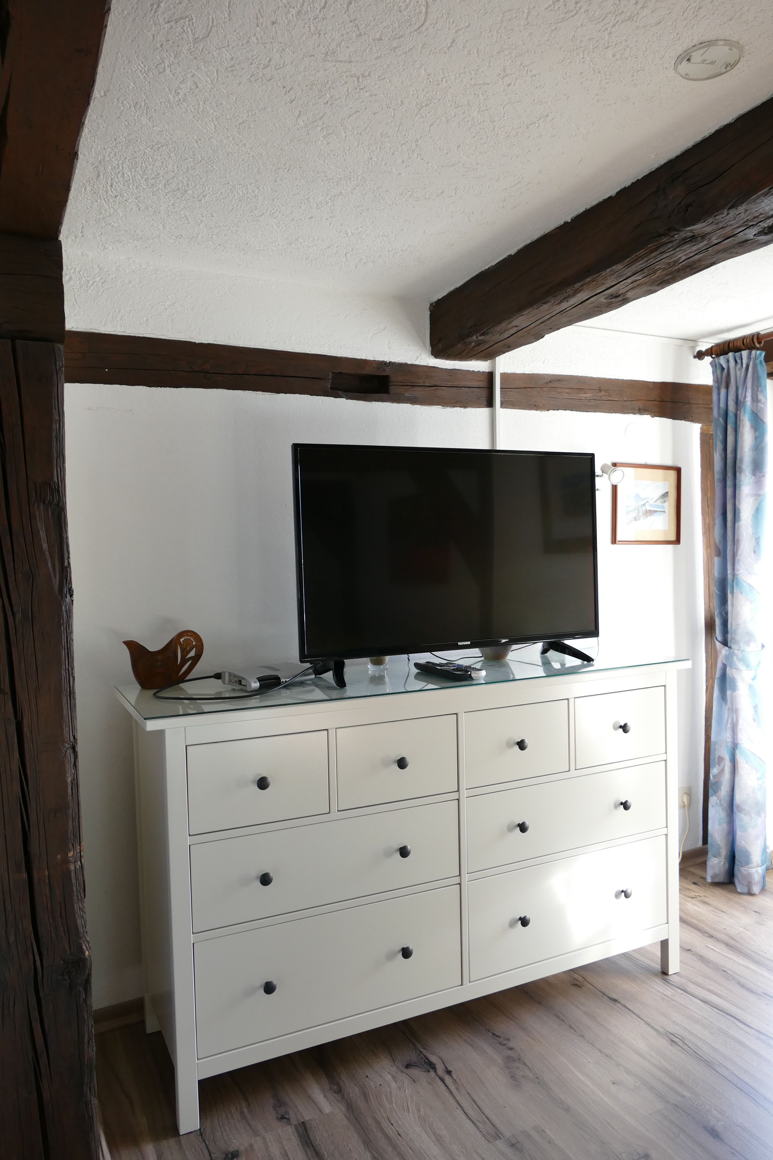 A white dresser with a flat-screen TV, drawers, and a decorative item on top.