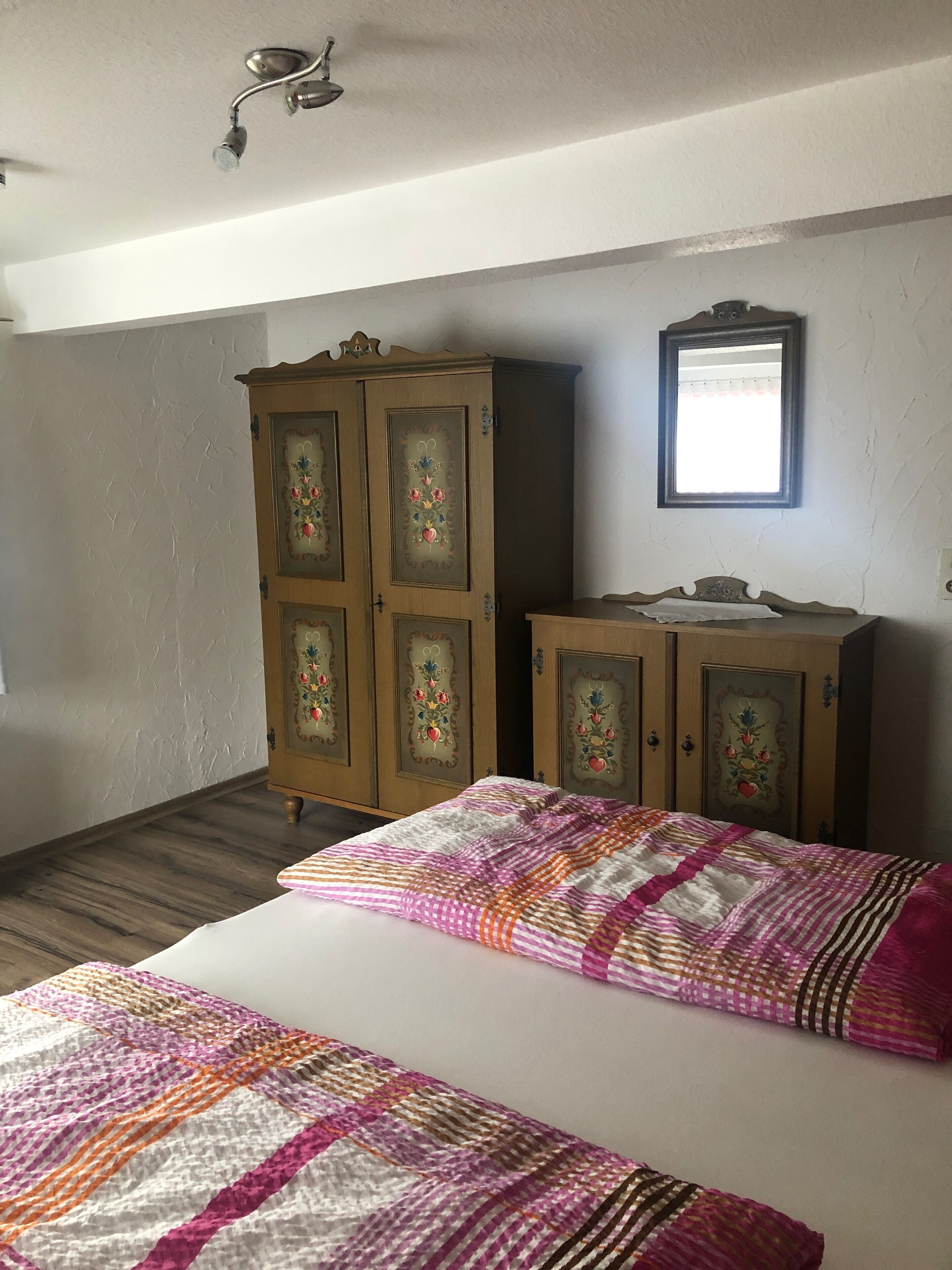 A bedroom with a wooden wardrobe, a bed with a colorful quilt, and a mirror on the wall.