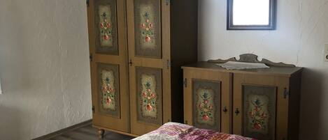 A bedroom with a wooden wardrobe, a bed with a colorful quilt, and a mirror on the wall.
