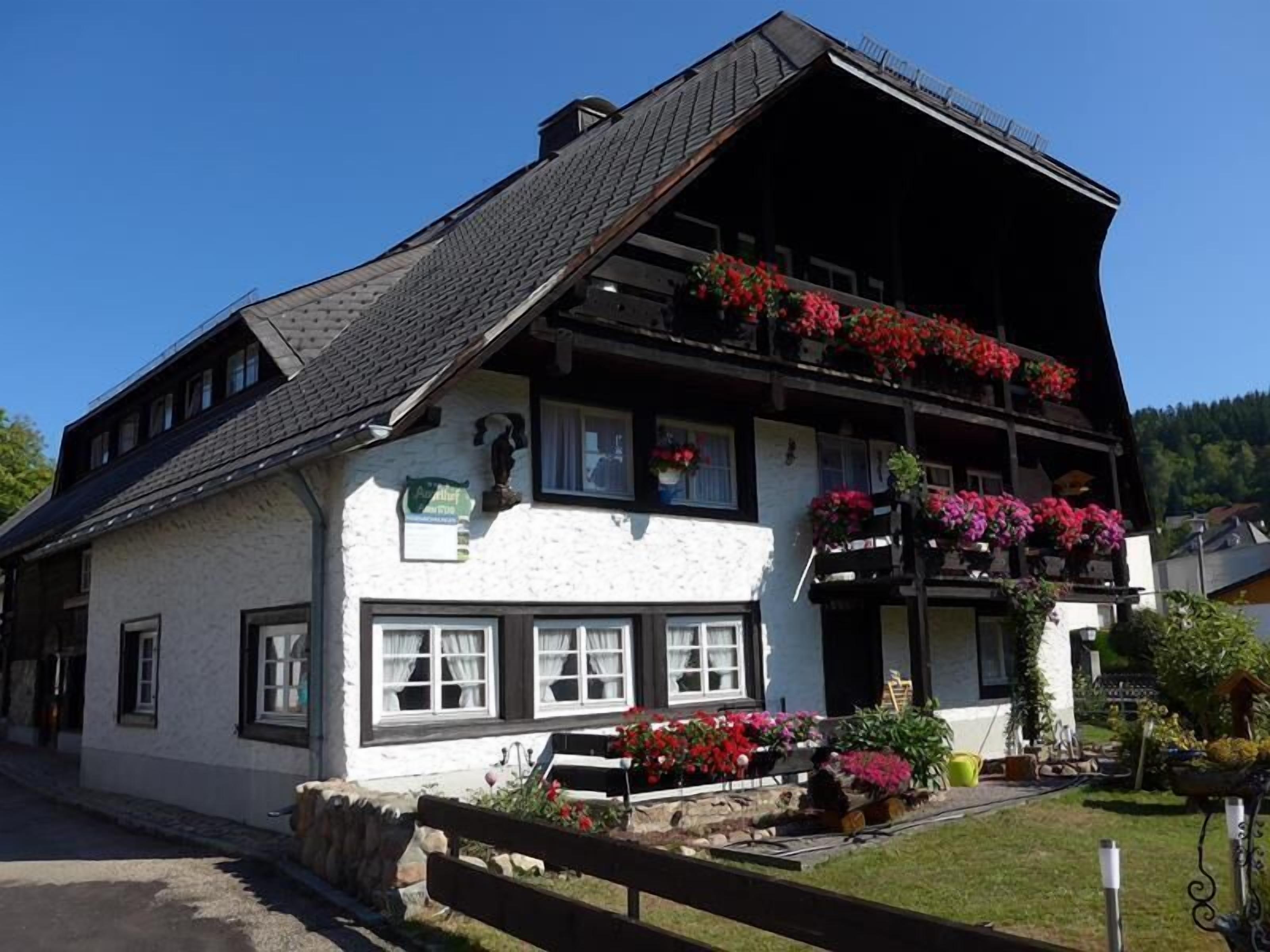 A traditional white building with a steeply pitched roof, multiple windows, and a balcony adorned with red flowers.