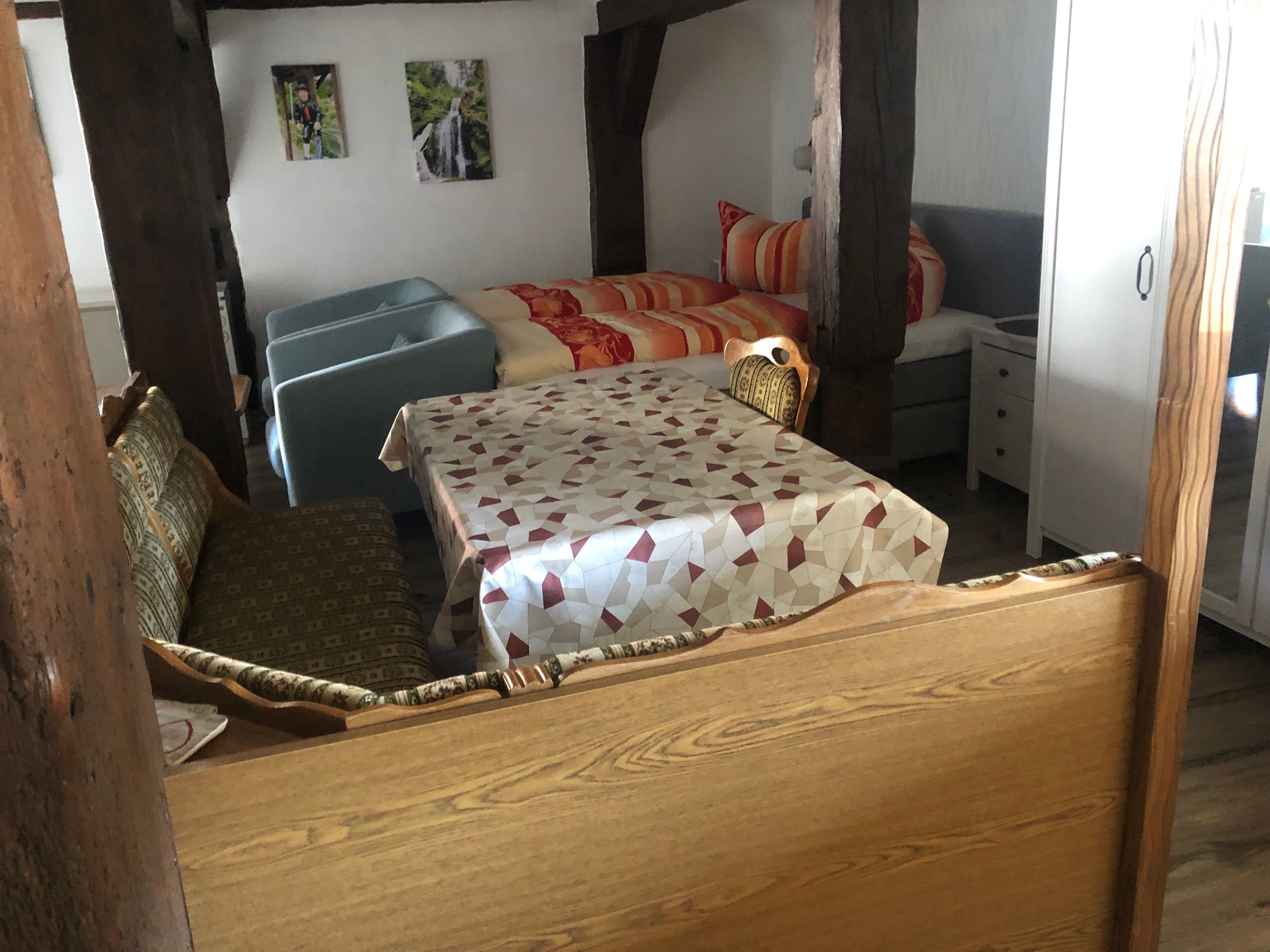 Un lit en bois avec une couvre-lit à motifs, une chaise bleue et une petite table avec un coussin.