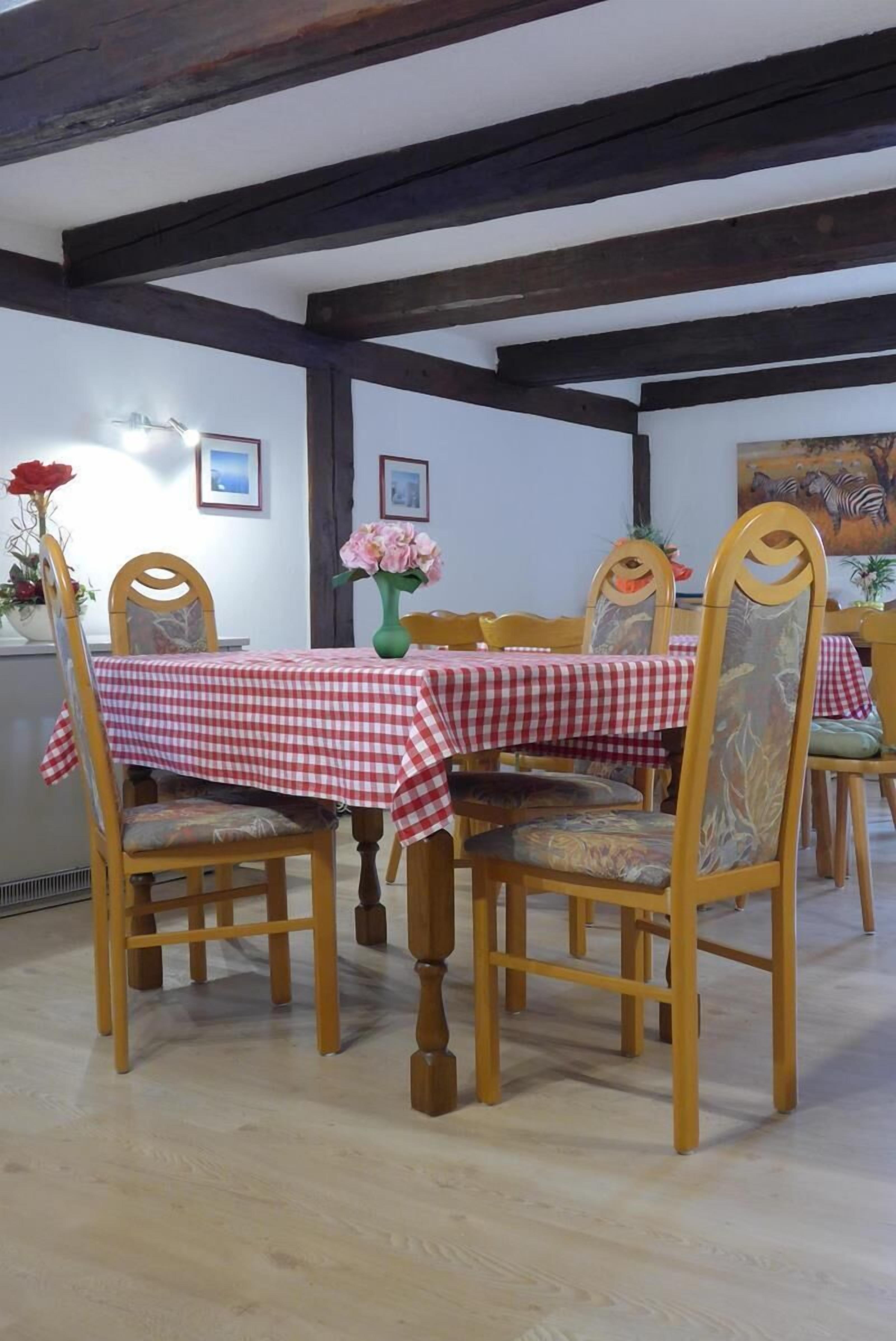 Un comedor con mantel a cuadros, sillas de madera y un jarrón con flores.