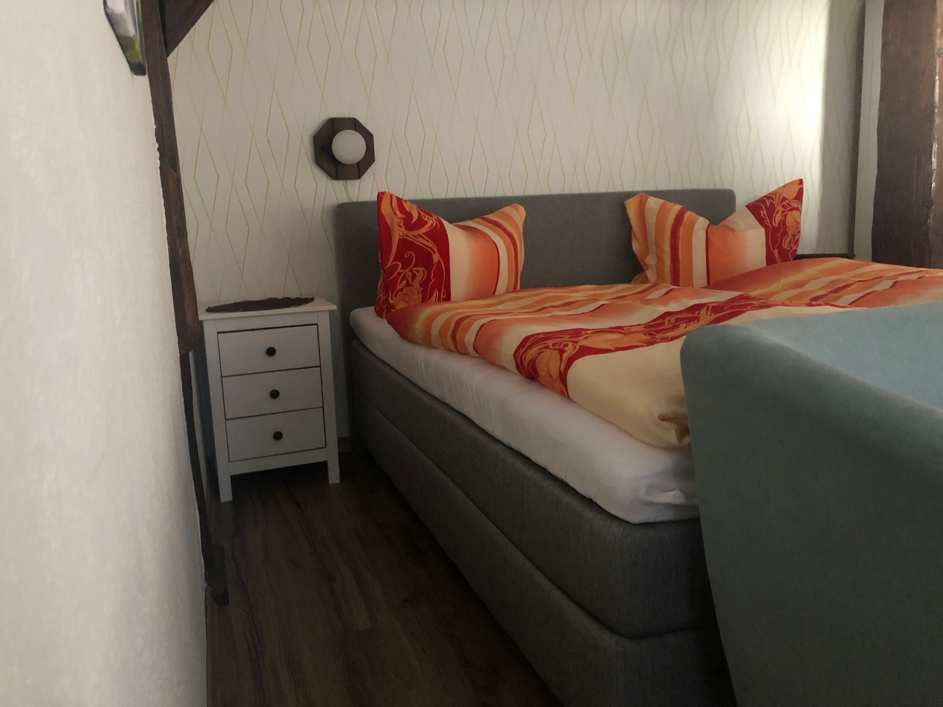 A bedroom with a bed, a nightstand, and a wall-mounted clock.