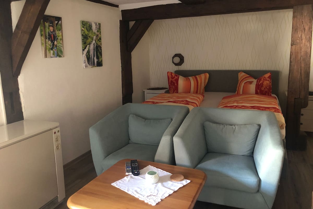 A cozy room with two beds, a sofa, a table with a cup and a cookie, and a refrigerator.