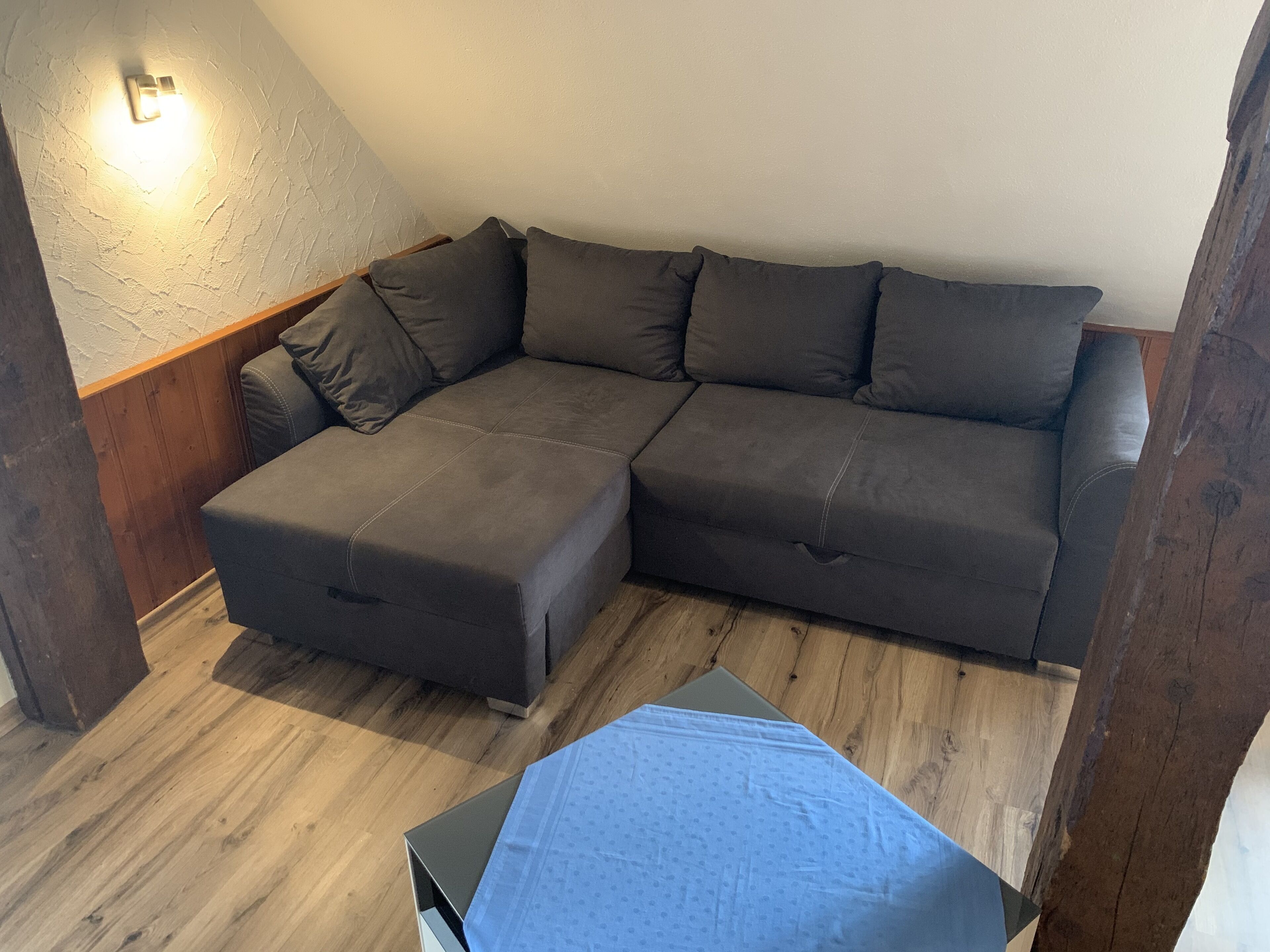 A sectional sofa with a wooden floor and a light switch on the wall.