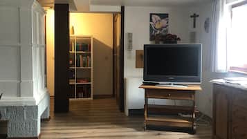 Een woonkamer met een houten vloer, een televisie op een dressoir, een boekenkast en een deur naar een andere kamer.