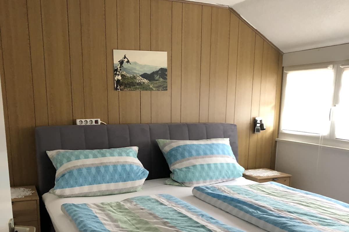 A bedroom with a large bed, wooden panel walls, a nightstand, a lamp, and a window.