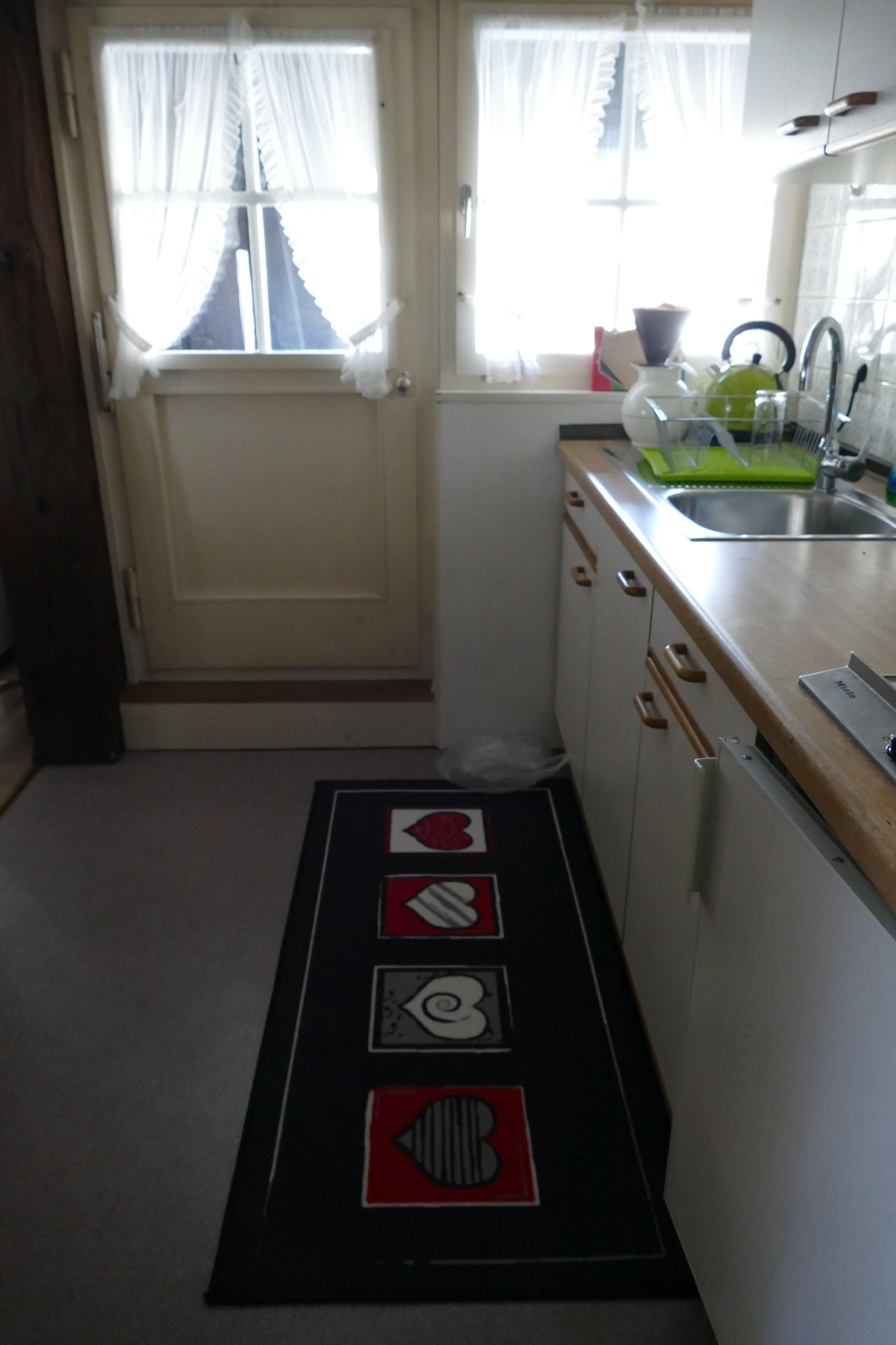 Een smalle keuken met een raam, een spoelbak en een mat met symbolen.