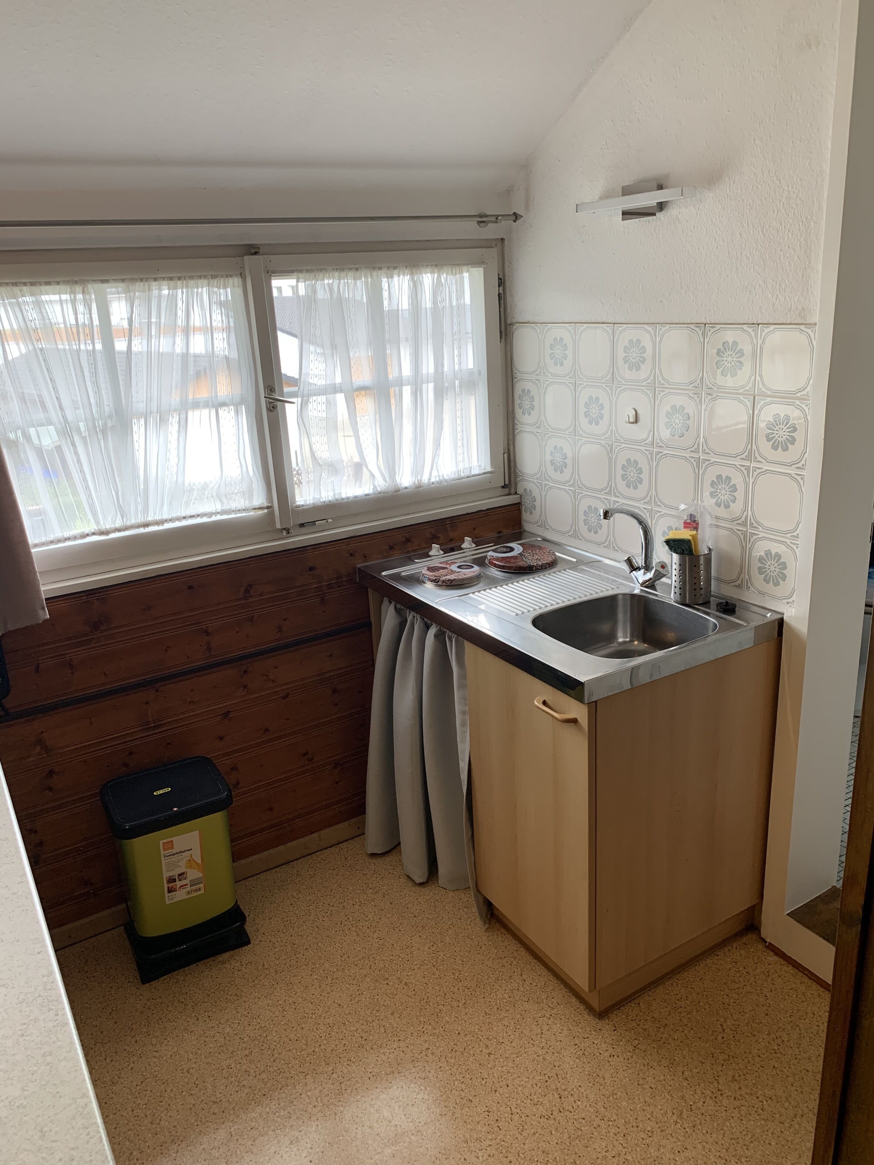 Cocina compacta con ventana, lavamanos y cubo de basura.