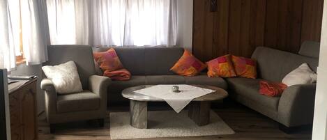 A living room with a wooden floor, a grey sofa, a grey armchair, and a round coffee table.