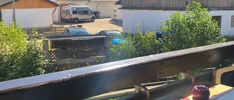 A balcony with a table and a chair, overlooking a residential area with houses and parked cars.