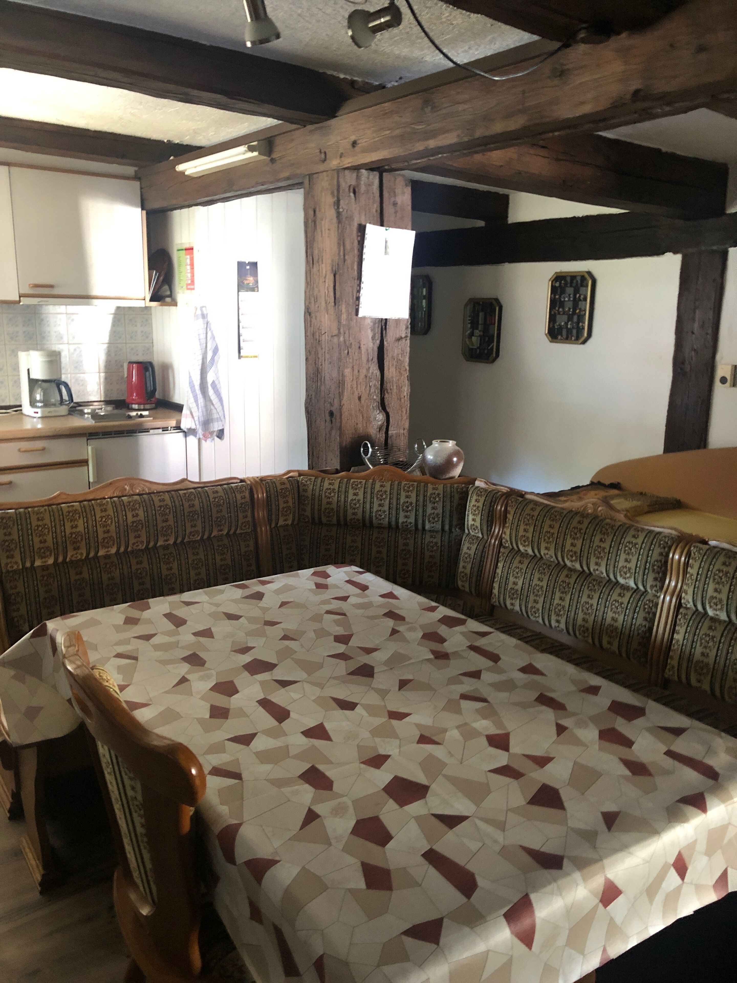 Una habitación con una cama grande, un banco de madera, una mesita y una kitchenette al fondo.