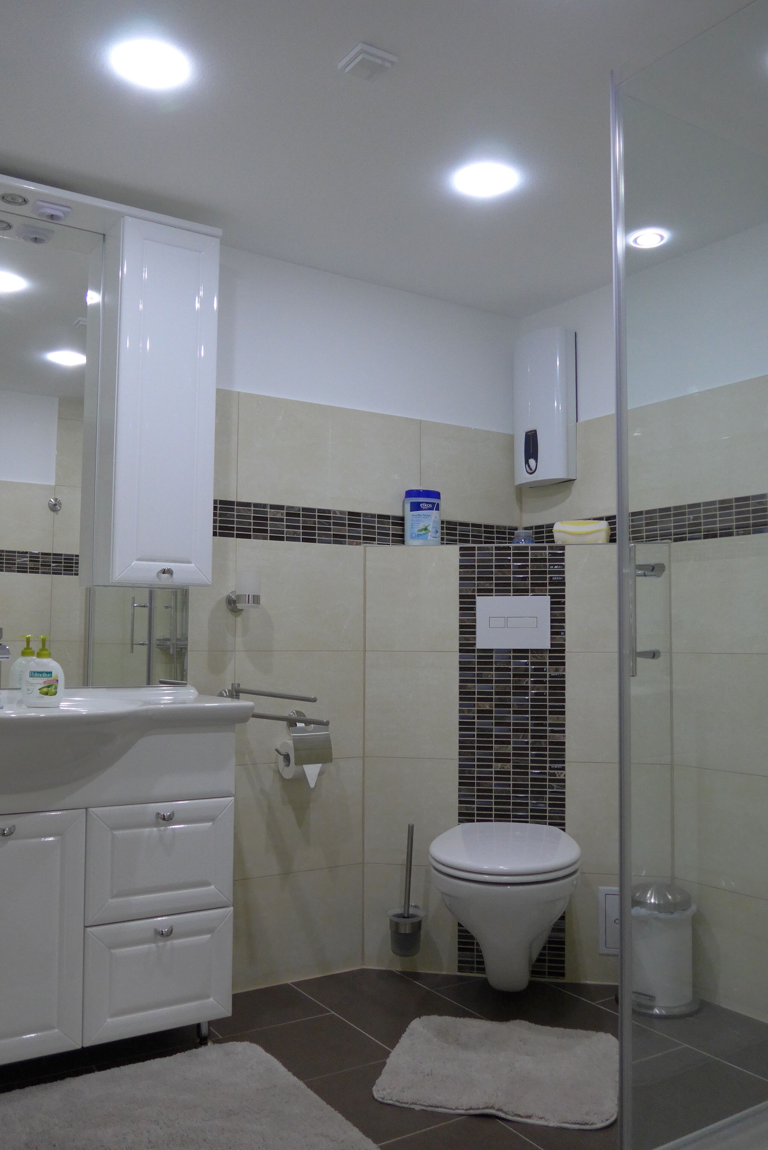 A modern bathroom with a white sink, mirror, and toilet. It includes a shower area with a glass door and a hand dryer.