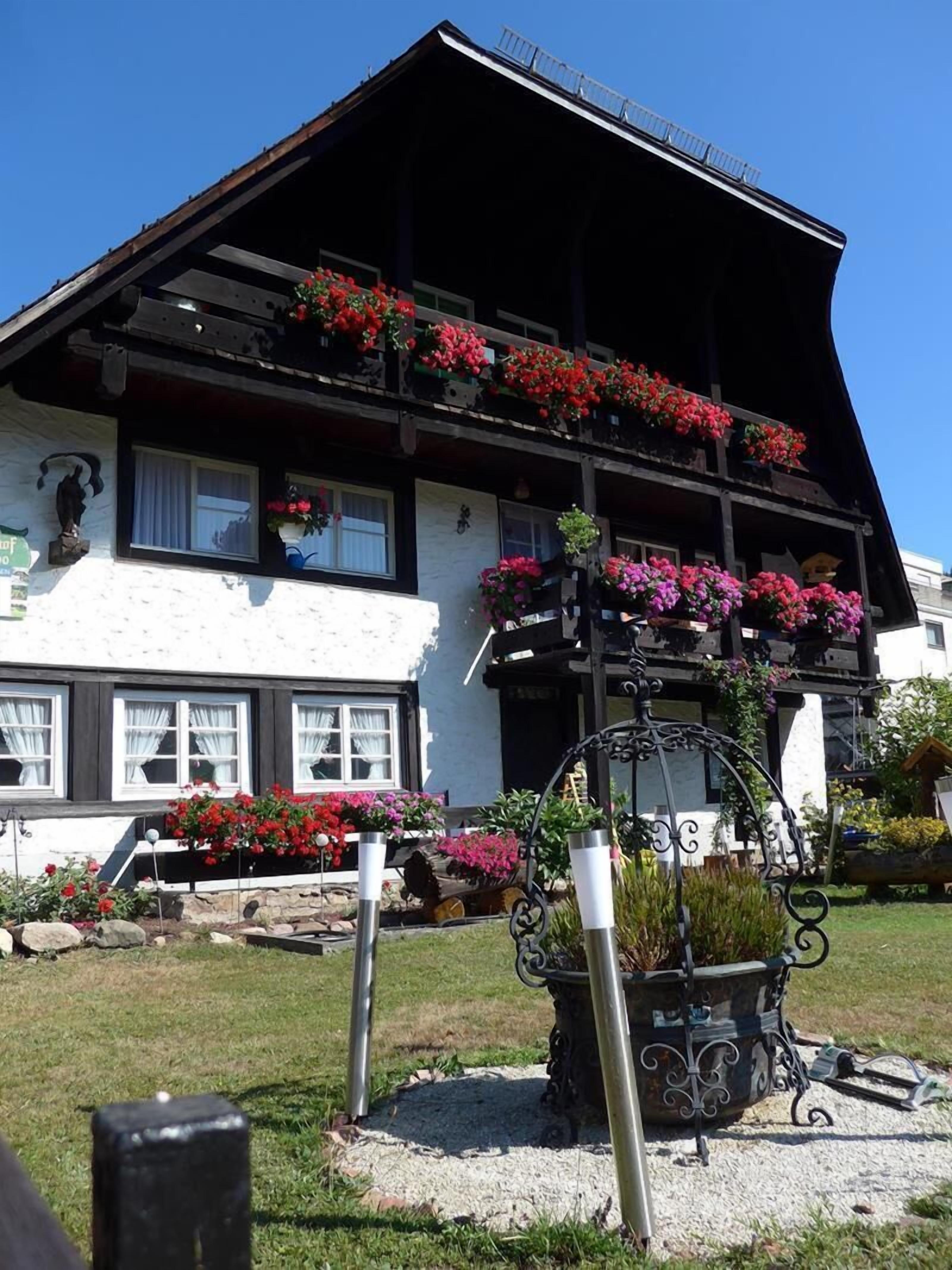 Una cabaña tradicional con techo inclinado, balcones con jardineras florales y un camino de entrada de grava.