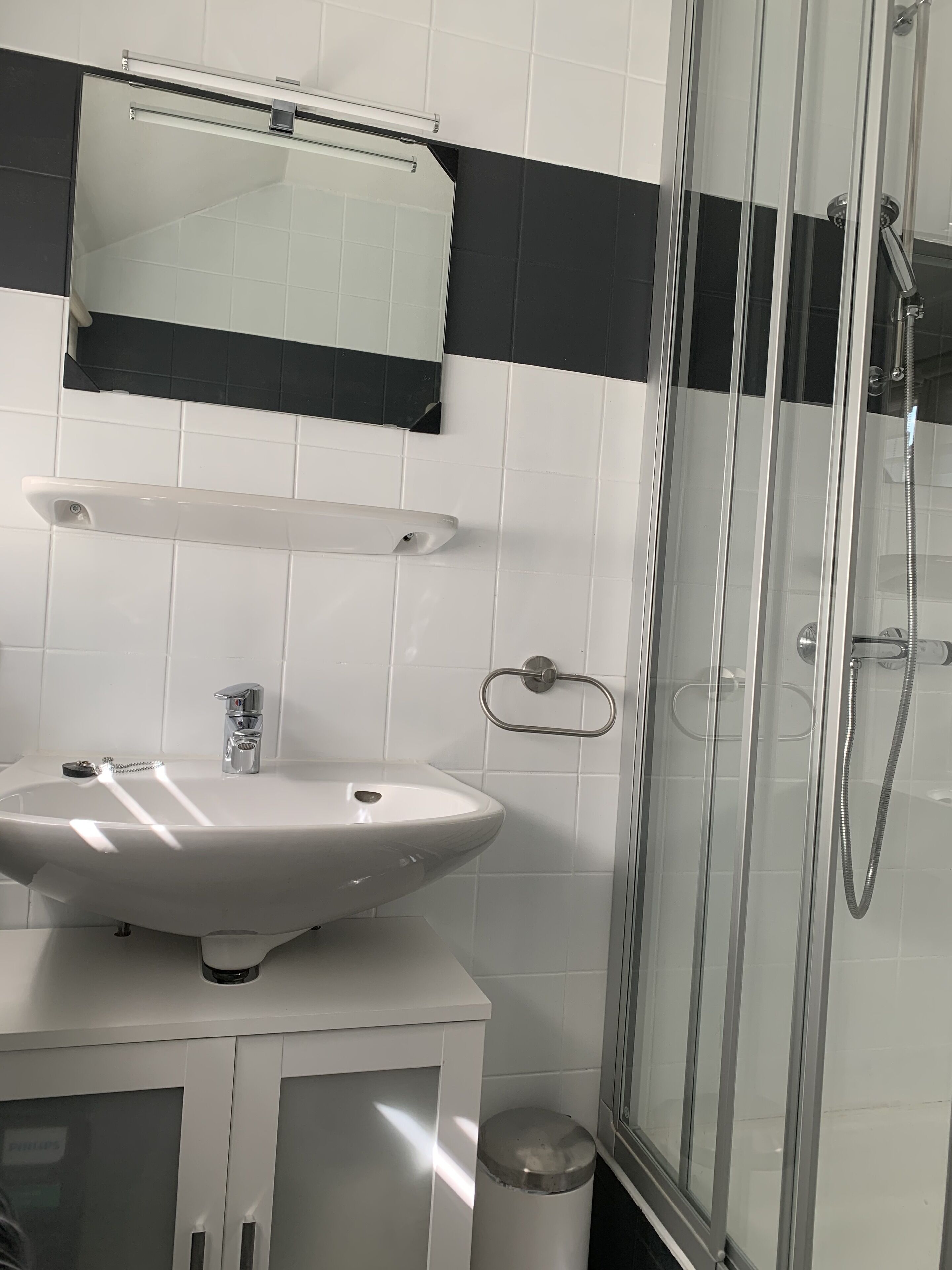 Un ba ño con lavamanos blanco, espejo y ducha con mampara de vidrio.