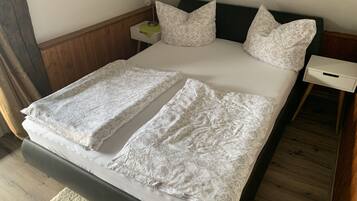 Una cama con cabecera de madera, sábanas blancas y dos almohadas. Hay una mesita de noche con una lámpara y un cajón.