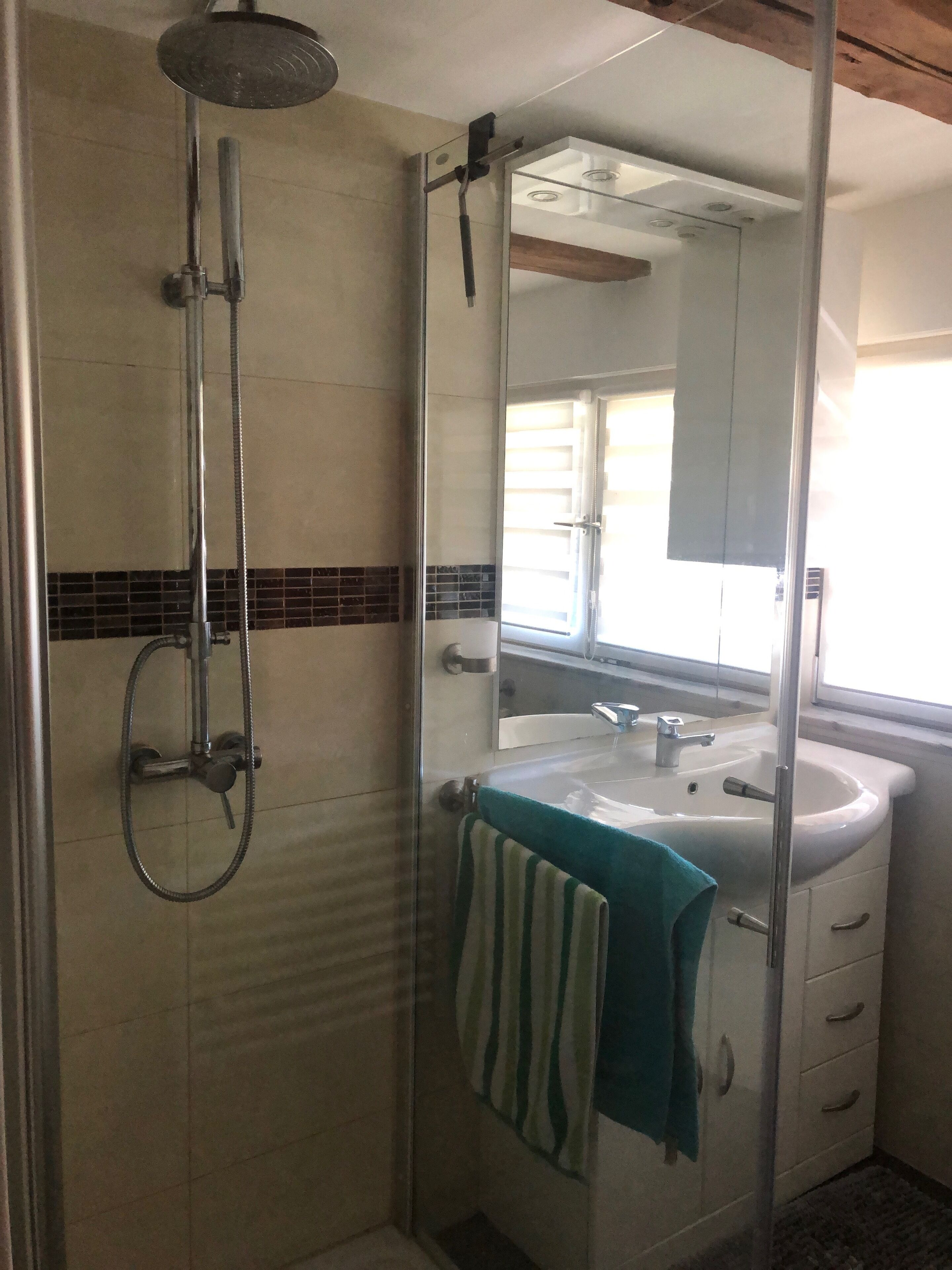 A bathroom with a glass shower enclosure, a sink with a mirror, and a towel hanging on the wall.