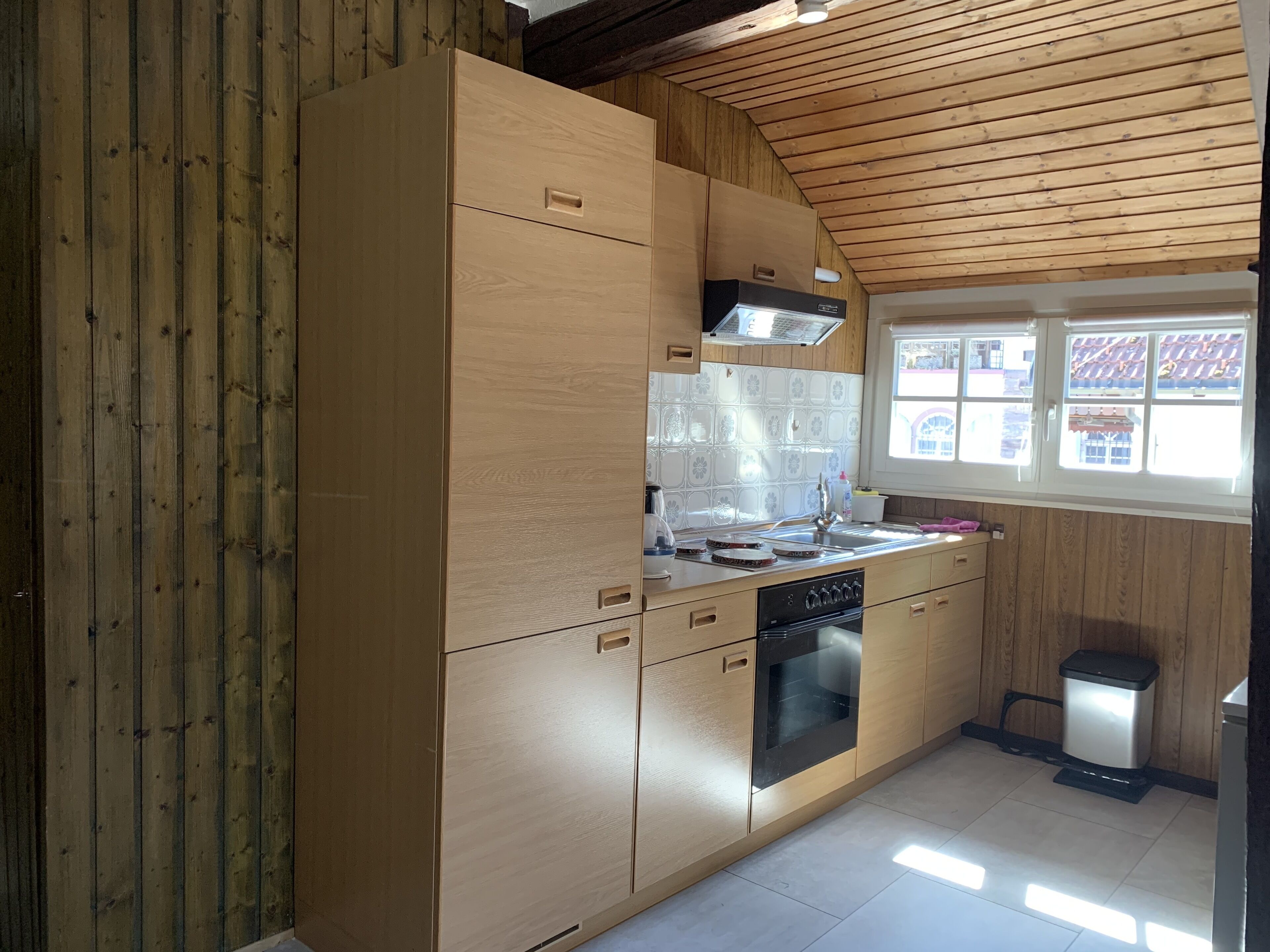 Une cuisine moderne avec des meubles en bois, un four encastré et une fenêtre donnant sur les bâtiments environnants.