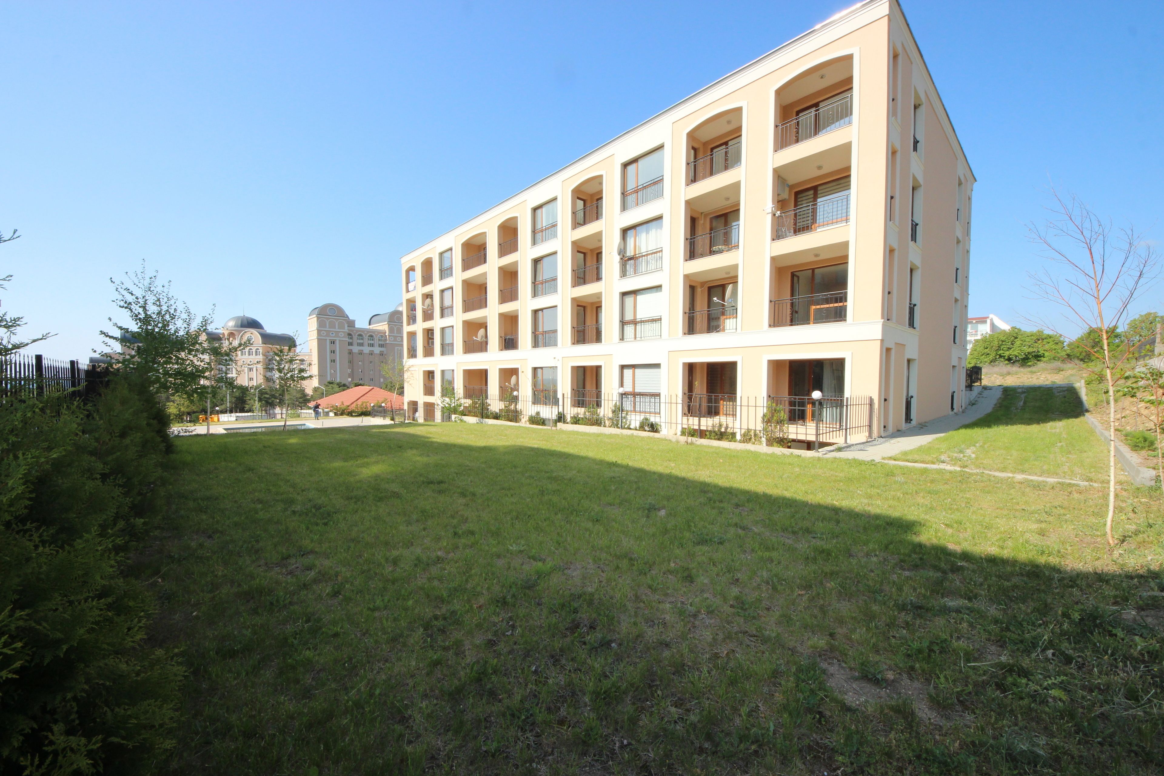 A multi-story building with balconies, a grassy courtyard, and a clear blue sky.