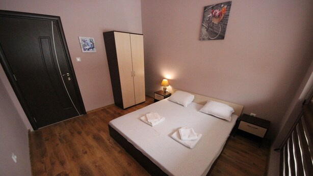Une chambre d’hôtel avec un plancher en bois, un lit avec du linge de lit blanc, une armoire, une table de chevet avec une lampe et un tableau accroché au mur.