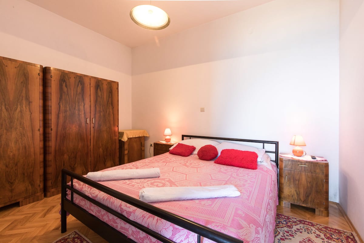 A bedroom with a bed, wooden wardrobe, bedside tables, and a ceiling light.