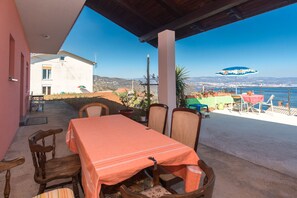 A terrace with a table and chairs, overlooking a scenic view of a coastal area with a clear sky. - Apartment Lucia & Holiday Home Nino (Opatija)