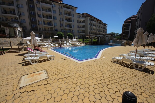 A pool area with lounge chairs and umbrellas, surrounded by multi-story buildings. - Menada Apartments in Sunny Beach Hills (Sunny Beach)