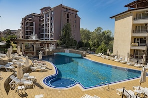 A swimming pool with lounge chairs and umbrellas, surrounded by buildings.