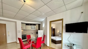 A compact living space with a kitchenette, a dining area with red chairs, a bed, and a TV mounted on the wall. - Menada Apartments in Sunny Beach Hills (Sunny Beach)