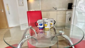 A glass-top dining table with four mugs featuring cartoon designs, set on red chairs in a modern kitchen. - Menada Apartments in Sunny Beach Hills (Sunny Beach)