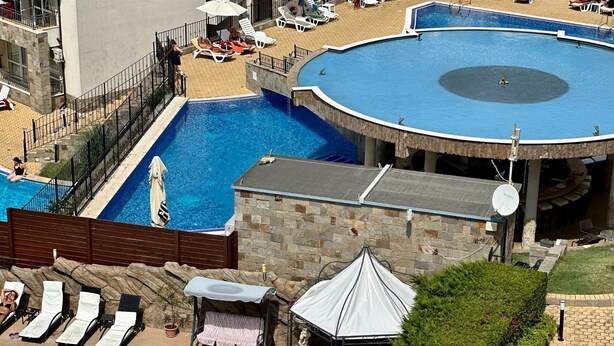 A large outdoor swimming pool with multiple sections, surrounded by lounge chairs and umbrellas. - Menada Apartments in Sunny Beach Hills (Sunny Beach)