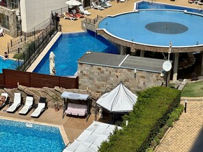 A large outdoor swimming pool with multiple sections, surrounded by lounge chairs and umbrellas. - Menada Apartments in Sunny Beach Hills (Sunny Beach)