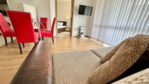 A modern living room with a sofa, red chairs, a flat-screen TV, and a wooden floor. - Menada Apartments in Sunny Beach Hills (Sunny Beach)